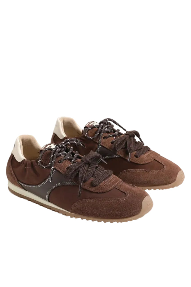 A pair of brown suede and leather sneakers with dark brown laces, a dark gray side stripe, and a beige outsole, photographed on a light gray studio background.