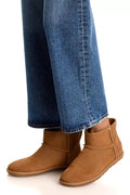 A person wearing brown suede ankle boots with blue jeans, shown from the calves down against a clean white background.