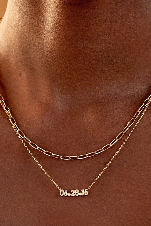Gold chain necklace with a date pendant on a person's neck against a neutral background