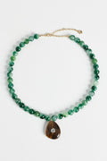 A green beaded necklace with a teardrop-shaped brown stone pendant featuring a small clear stone, displayed on a clean white background.