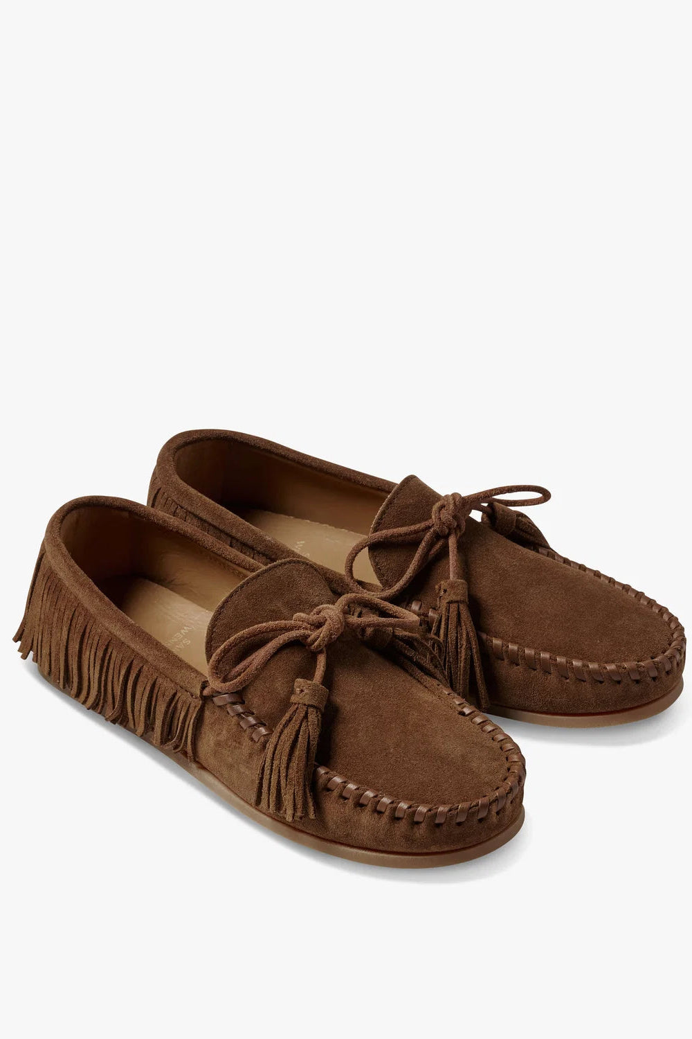 A pair of brown suede moccasin-style slip-on shoes with fringe trim and tassel details, photographed on a clean white background.