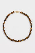 A beaded necklace made of round brown and black tiger's eye beads with a small gold clasp, displayed on a clean white background.