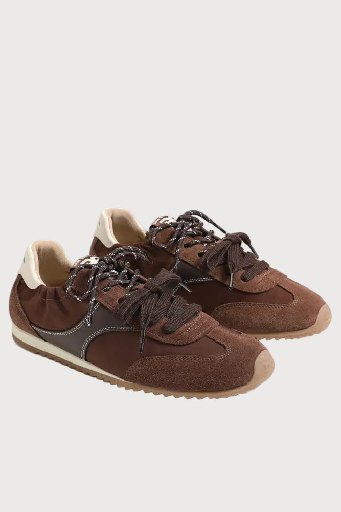 A pair of brown suede and leather sneakers with dark brown laces, a dark gray side stripe, and a beige outsole, photographed on a light gray studio background.