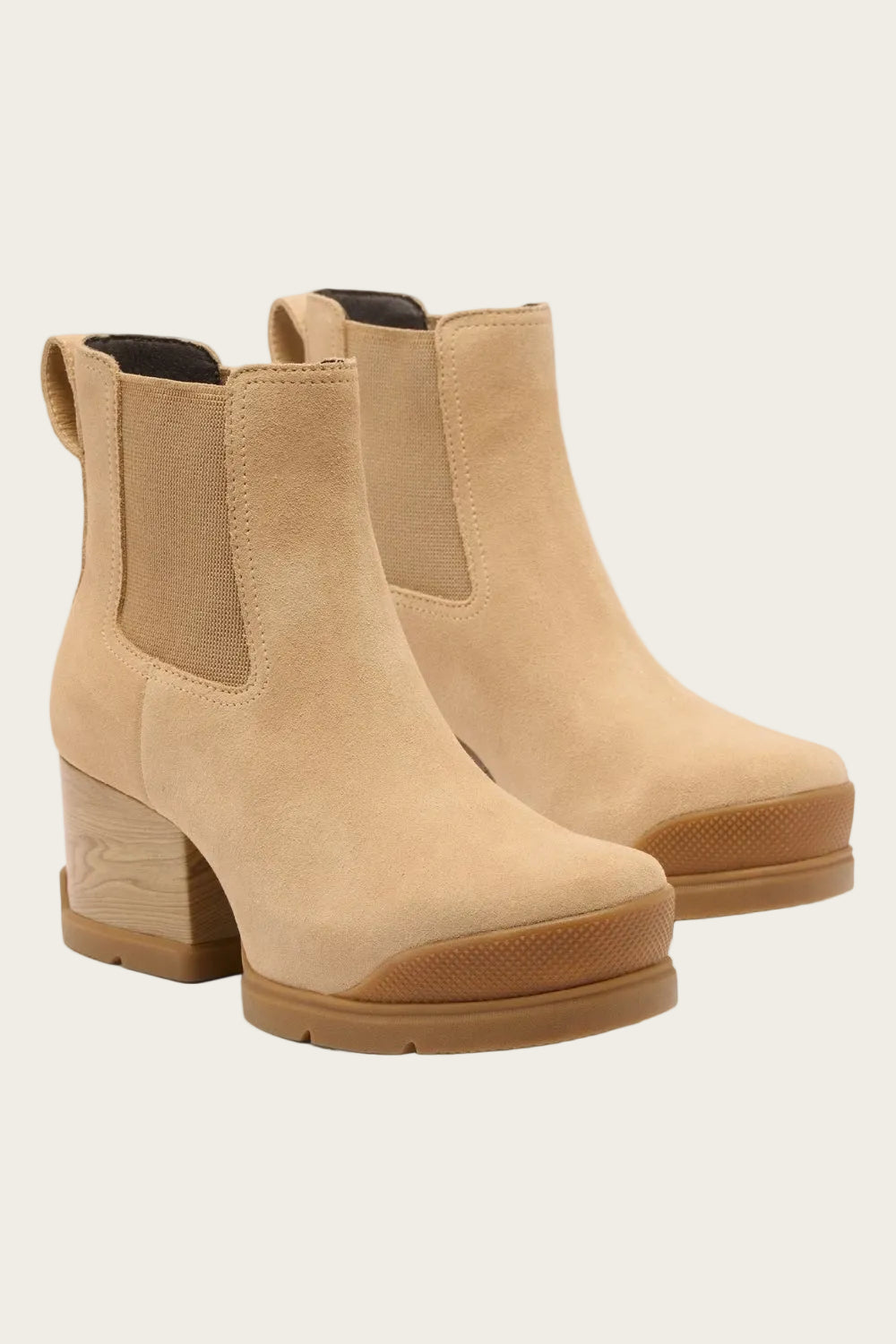 A pair of beige suede Chelsea-style ankle boots with elastic side panels, a stacked wood-look block heel, and a gum sole, shown on a light gray background.